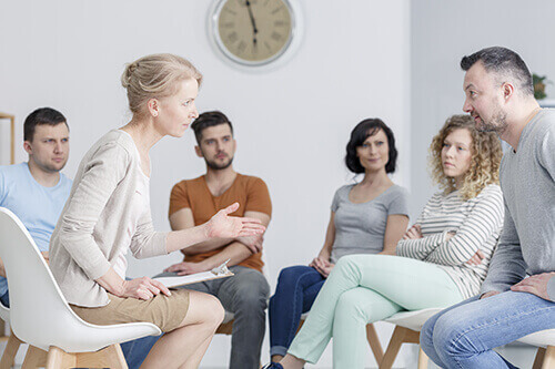 Woman explains to a group of individuals what a cognitive behavioral therapy program is