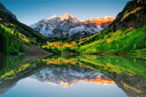 sunrise over a Colorado lake with lush forest and snowy mountain peaks in the background